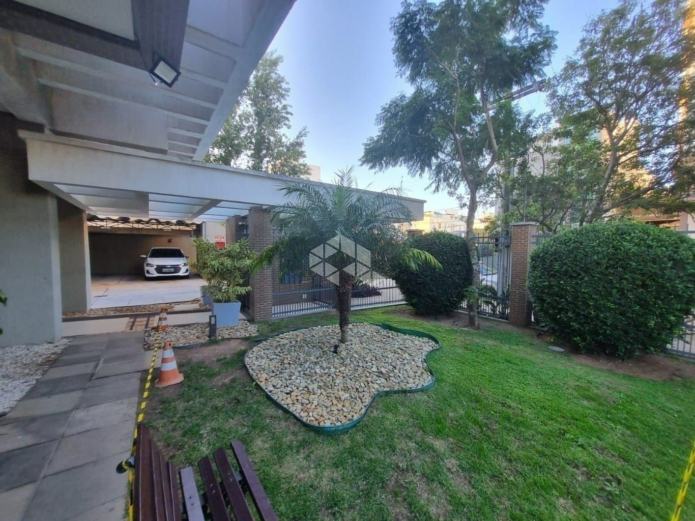 Área externa de acesso com jardim gramado, árvores e garagem ao fundo